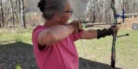 Women with pink shirt ready to shoot a bow and arrow at an outdoor archery range.