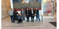 Group of women with one wheelchair user in front of a painting at a museum.