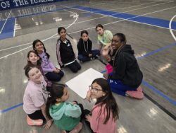 Small group of girls with a young women leader making a poster on a gym floor