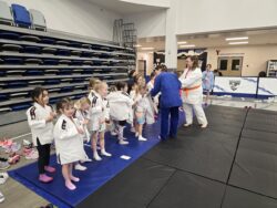 Group of young girls on a blue mat putting on a karate gi