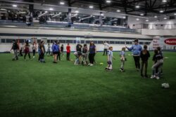 Group of young who are softball players on an indoor turf listening to their female coach.