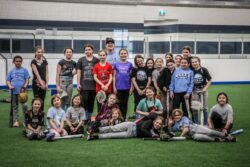 Group picture of a youth girls softball team and their coach on indoor turf.