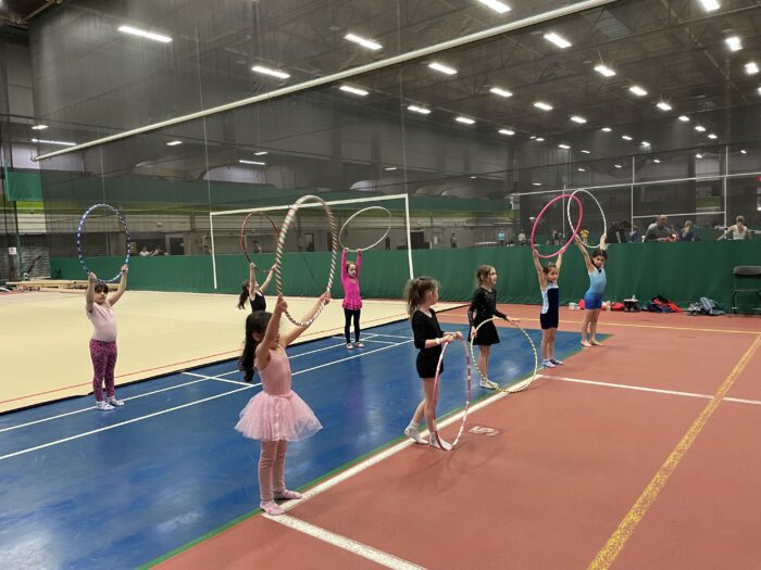 Group of young girls in an indoor fieldhouse holding a hoop above their head.
