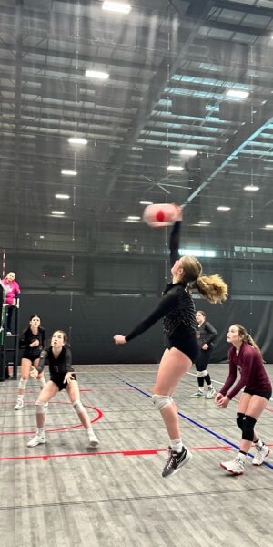 Teen girls playing volleyball in a gym.