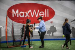 Women coach with teaching a young girl how to hold a softball bat.