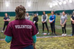 Women wearing a burgundy tshirt with volunteer on the back talking to a group of women holding frisbee discs for golf.