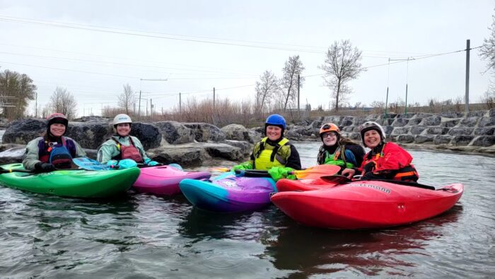 Five women in kayak gear posing for a picture on a river.