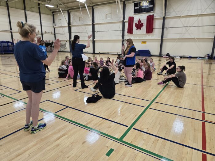 Group of girls in a gymnasium sitting listening to instructors.