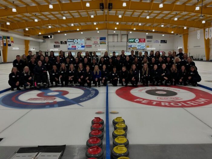 Group of women posing for a group picture on ice in a curling arena.