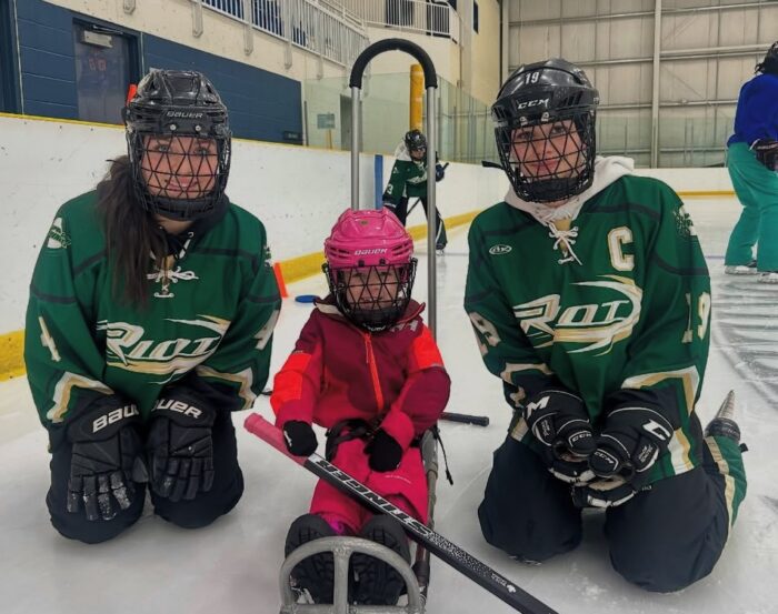 Two older girls kneeling beside a sledge skater.